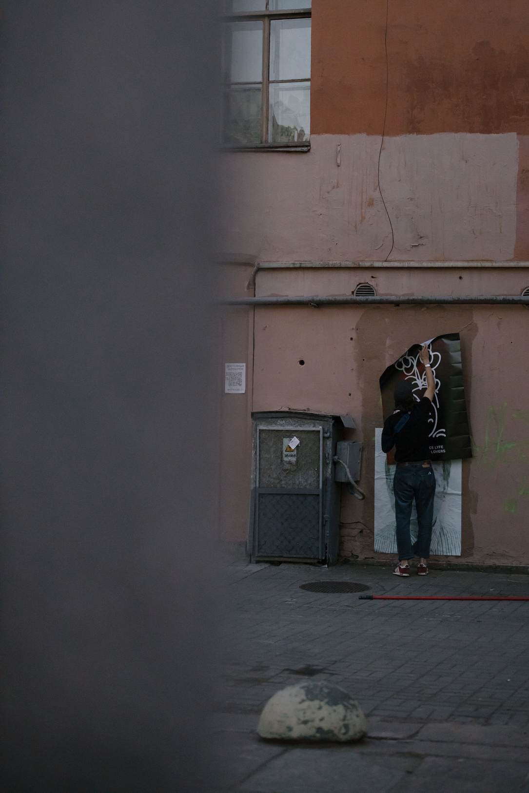 Man in Black Jacket and Blue Denim Jeans Standing Beside Gray Steel Door
